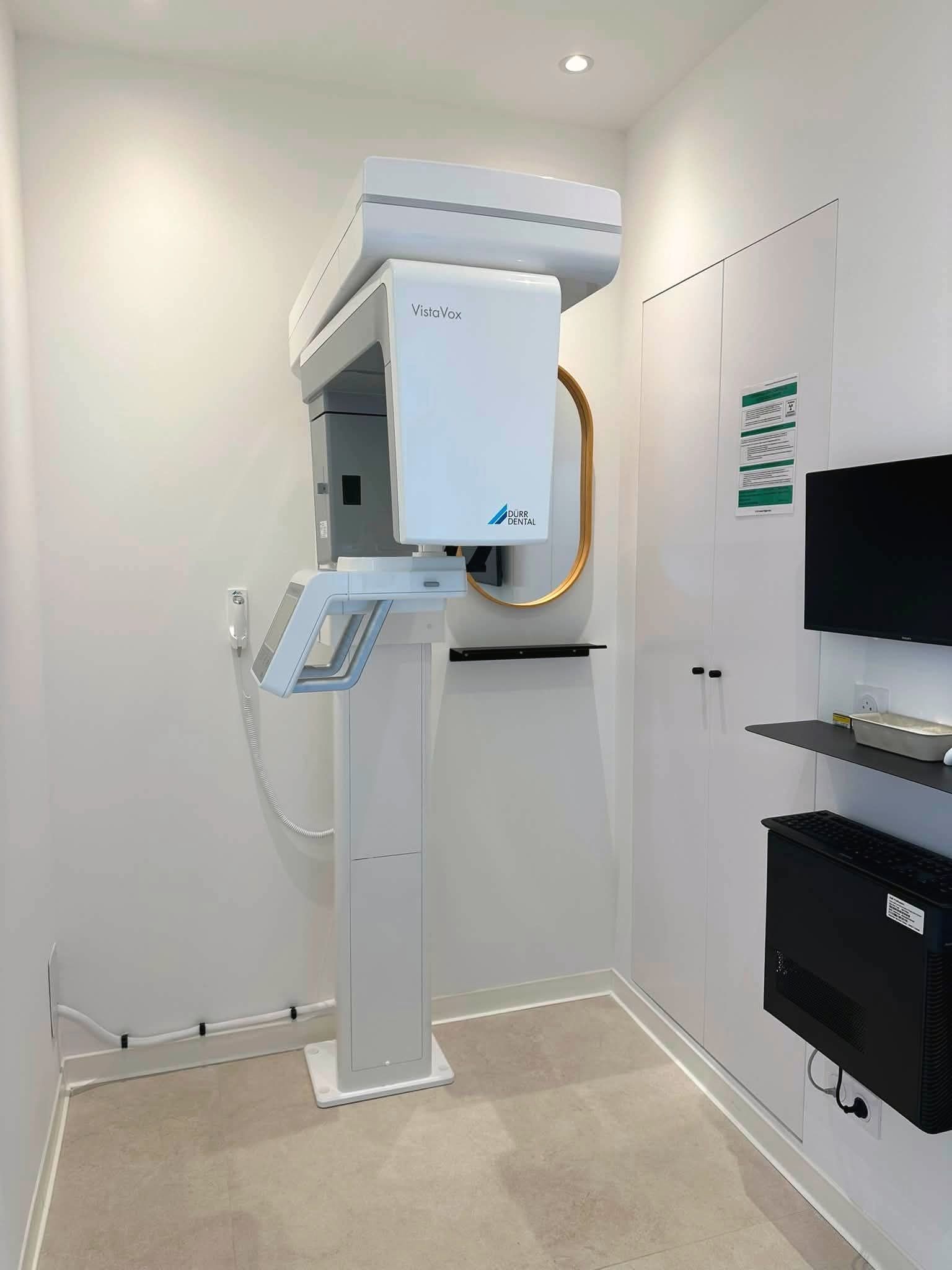 Appareil de radiographie panoramique blanc dans une petite pièce claire, à côté d’un miroir ovale cerclé de laiton.