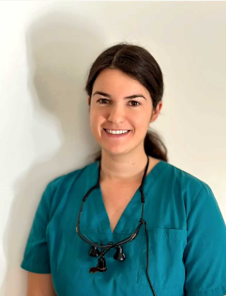 Portrait du Dr Jeanne Rigal, souriante, en tenue de soin bleu sarcelle, loupes binoculaires autour du cou.