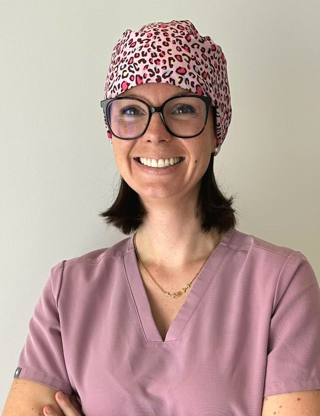 Portrait de Juliette, assistante dentaire, souriante, en tenue de soin rose et calot imprimé.