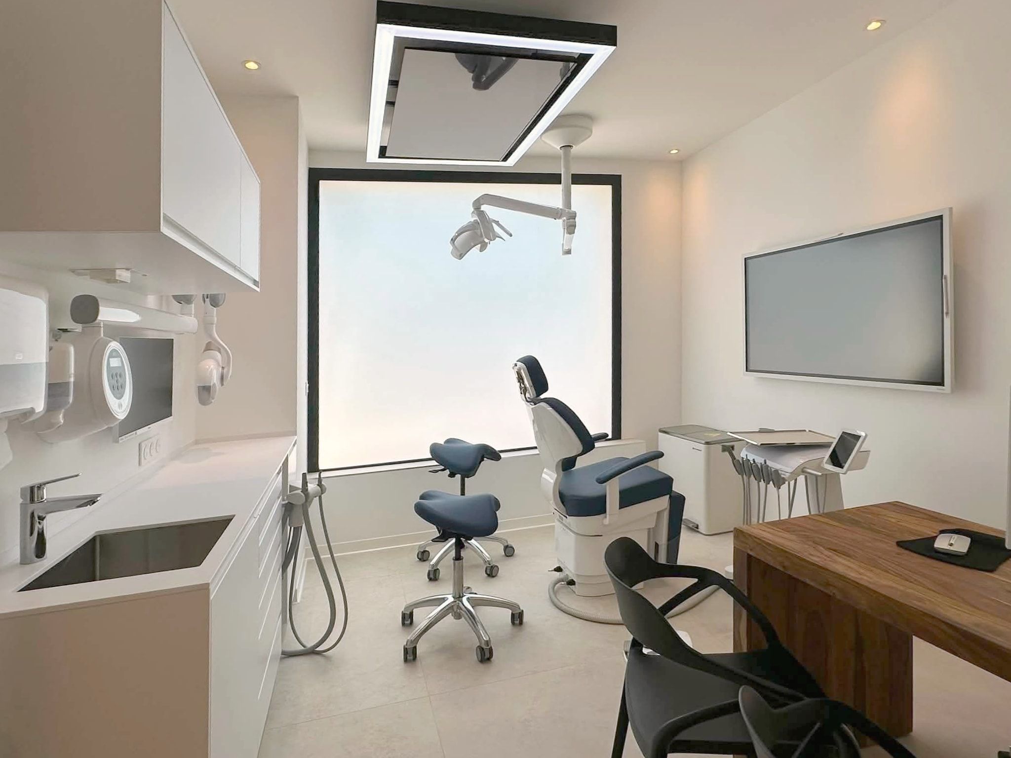 Seconde salle de soins : fauteuil bleu nuit devant une grande baie dépolie, écran au plafond, grand écran tactile au mur et bureau en noyer.